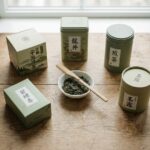 Comparatif de plusieurs marques de thé vert en feuilles et en boîtes sur une table en bois clair