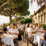 Vue panoramique d'une terrasse de restaurant ensoleillée en Nouvelle-Aquitaine avec des tables dressées sous les arbres et une ambiance estivale animée