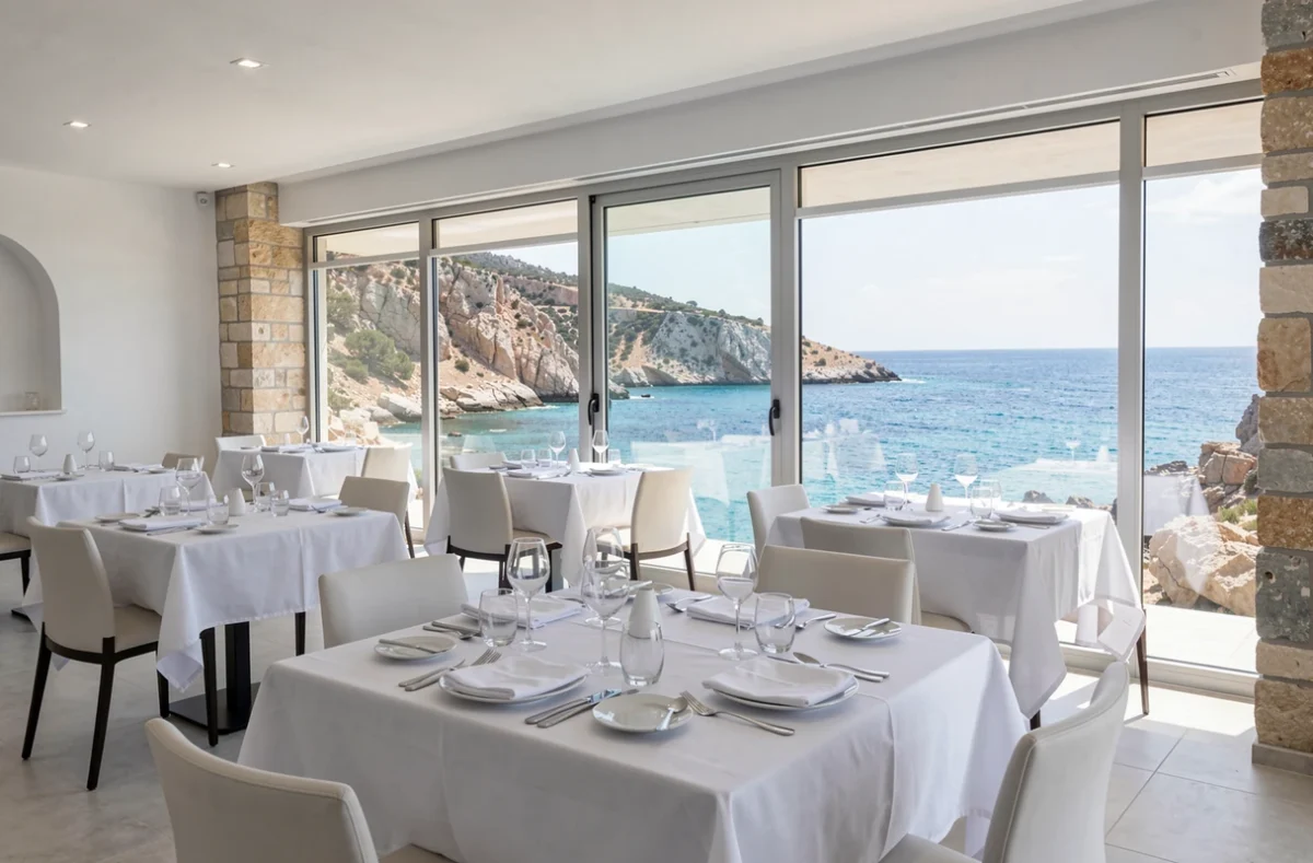 Salle de restaurant de La Villa Madie près de Cassis avec grandes baies vitrées offrant une vue panoramique sur la côte rocheuse méditerranéenne et une table dressée pour un dîner romantique
